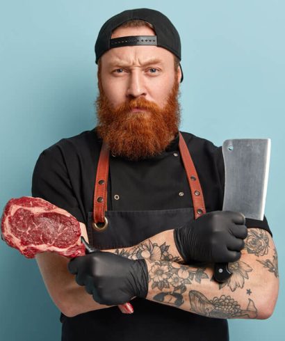 man-with-ginger-beard-apron-gloves-holding-knife-meat